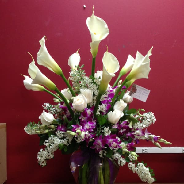 Tall bouquet of white calla lilies, white roses, and purple orchids in a glass vase