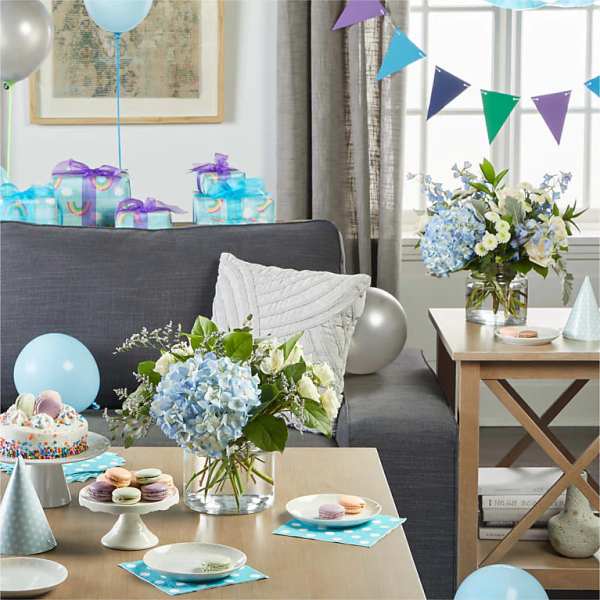 Blue and white floral arrangements on tables at a party with balloons and gifts.