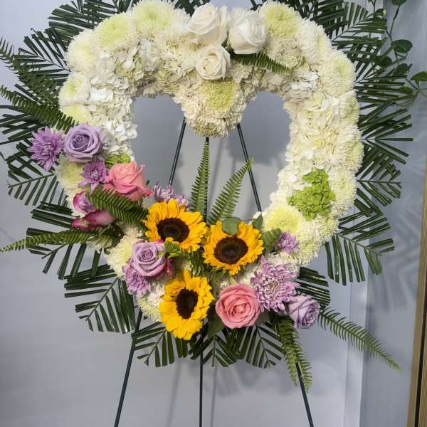 Heart-shaped floral wreath on an easel with white, pink, purple, and yellow flowers