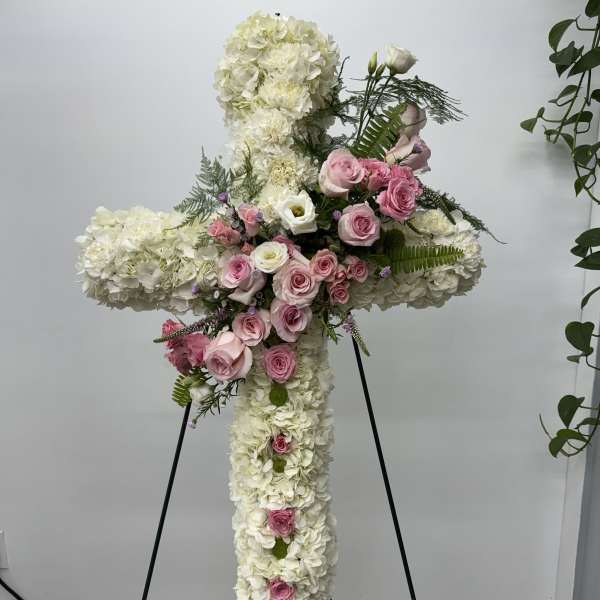 Large white floral cross with pink roses on a stand