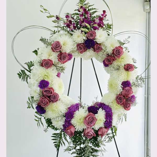Large floral wreath on a stand with pink roses, white mums, and purple flowers