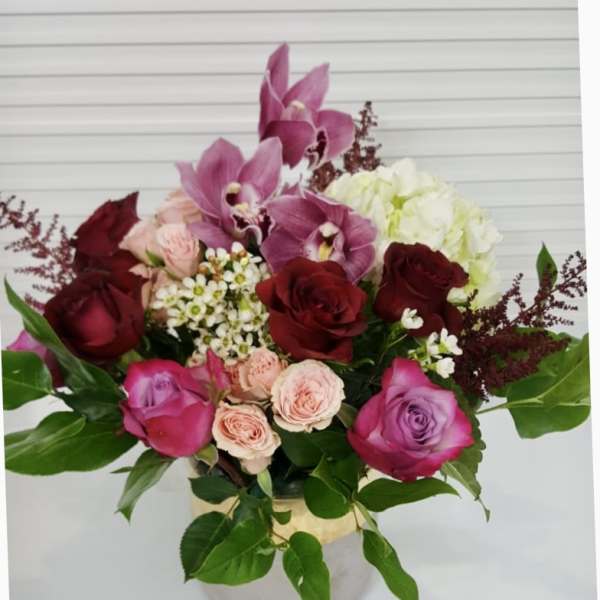 Bouquet of pink orchids, red and pink roses, and white hydrangea in a vase