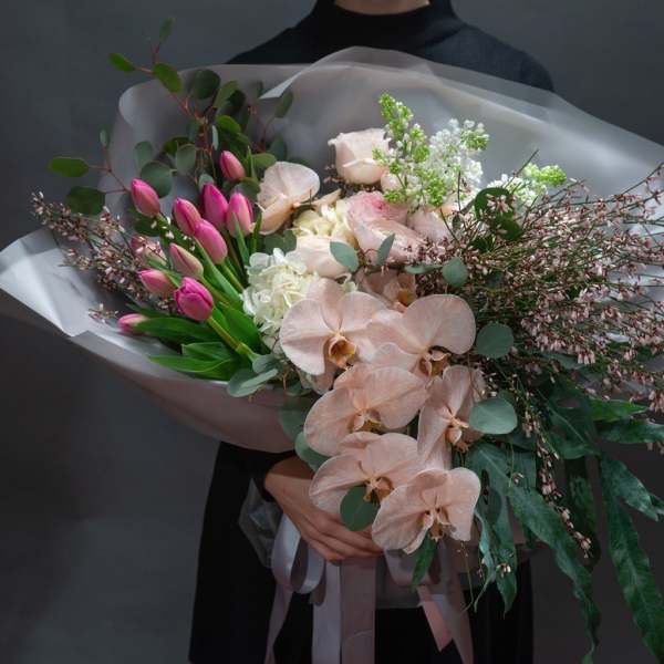 Bouquet of pink tulips, pale roses, and peach orchids wrapped in translucent paper