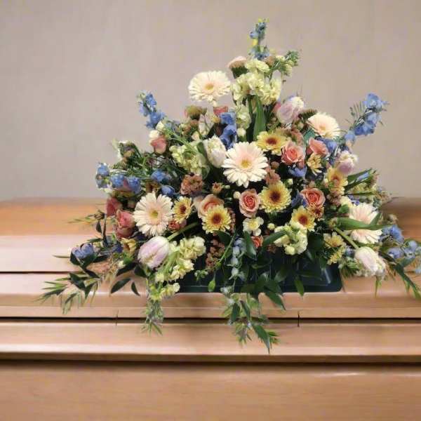 Floral arrangement on a casket with pastel flowers and blue accents