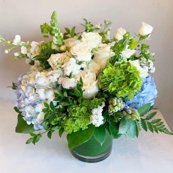 White roses and blue hydrangeas in a green glass vase