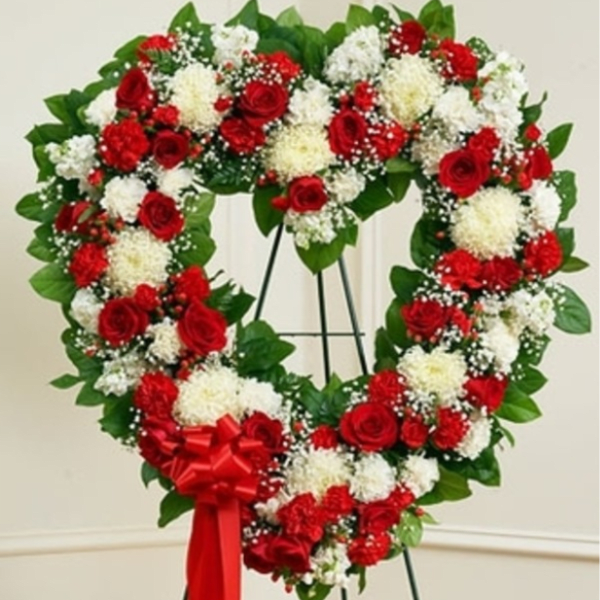 Heart-shaped wreath of red and white flowers on a stand with a red bow
