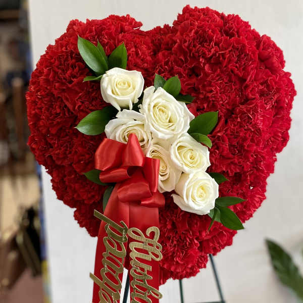 Heart-shaped red carnation arrangement with white roses and a red ribbon