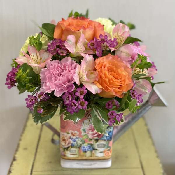 Bouquet of orange roses, pink carnations, and purple filler flowers in a decorative vase