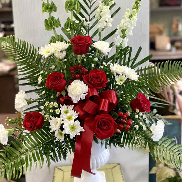 Red roses and white flowers in a white vase with a red ribbon