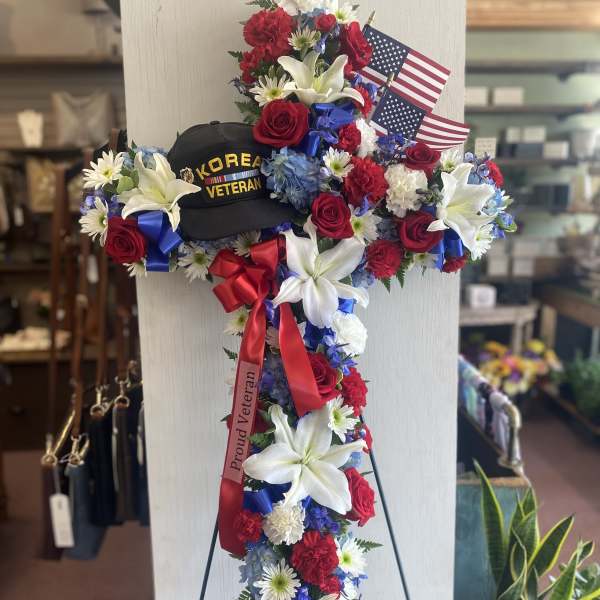 Floral standing cross with red, white, and blue flowers and small American flags