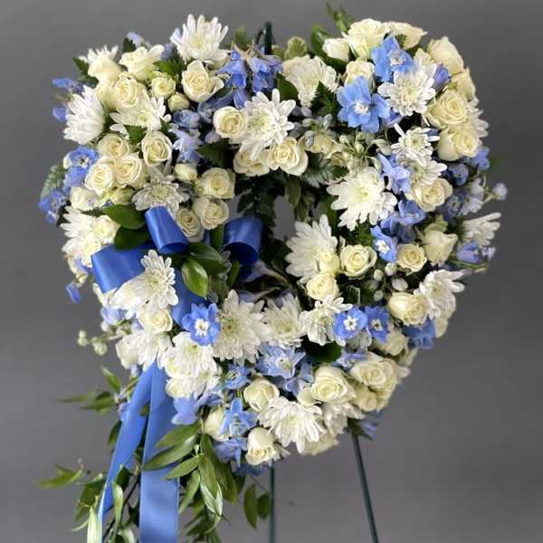 Heart-shaped wreath of white and blue flowers with a blue ribbon