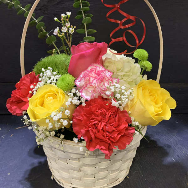 Basket arrangement of colorful roses and carnations with a red ribbon bow