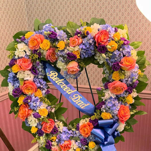 Heart-shaped floral wreath with a blue memorial ribbon on a stand