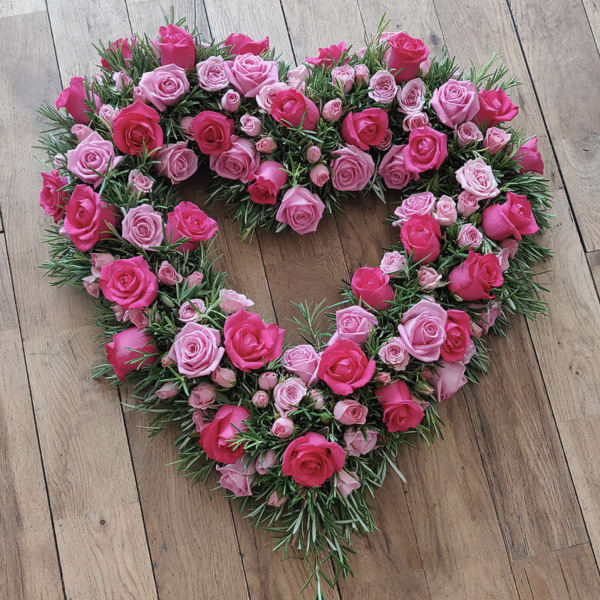 Heart-shaped rose arrangement in pink tones on a wooden floor