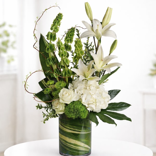 White lilies and roses arranged in a green glass vase