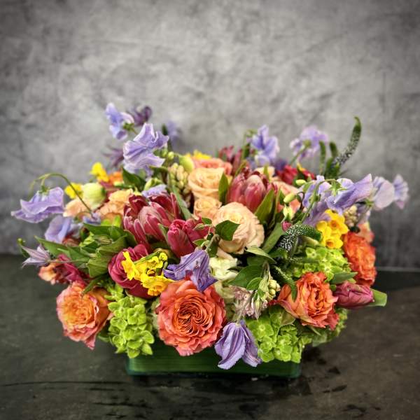 Mixed bouquet of coral, pink, yellow, and lavender flowers in a low container