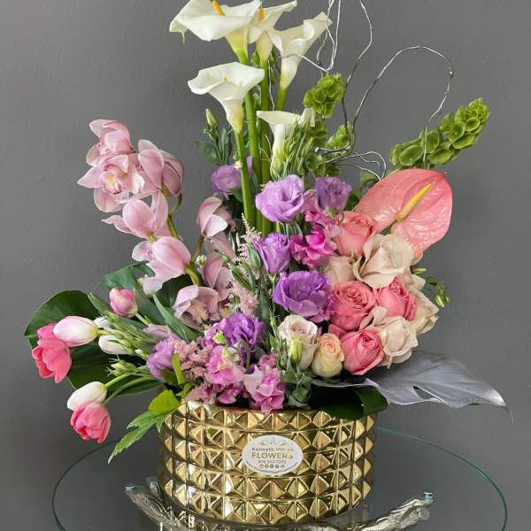Mixed bouquet with white calla lilies, pink orchids, and roses in a gold vase