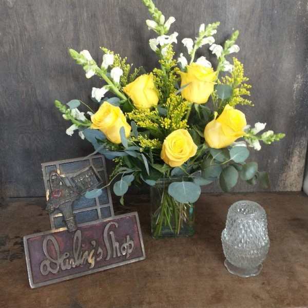 Yellow roses in a glass vase with white snapdragons and a small glass candle holder
