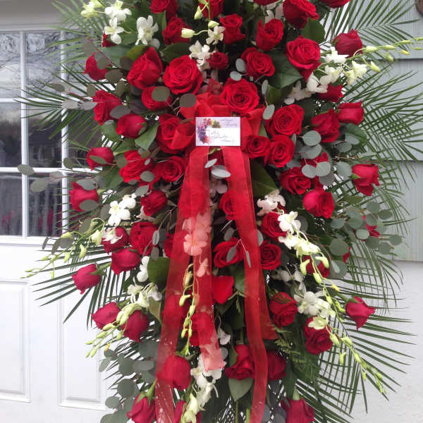 Tall standing spray of red roses with white orchids and a red ribbon