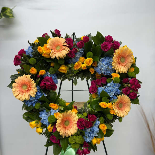 Heart-shaped floral wreath with roses, gerberas, and hydrangeas on a stand