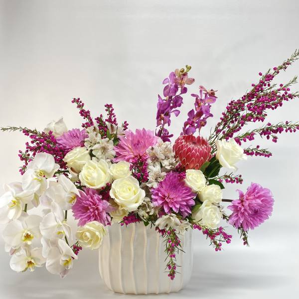 Mixed bouquet of white orchids, cream roses, pink dahlias, and purple orchids in a white vase