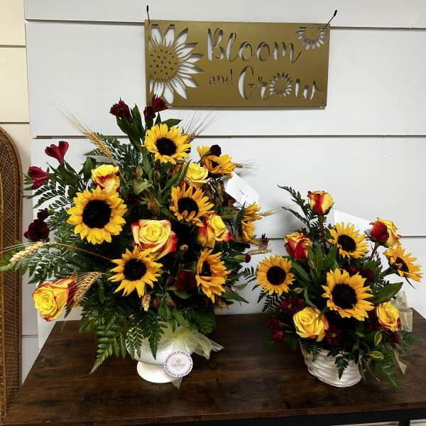 Two sunflower and rose arrangements in white containers on a table