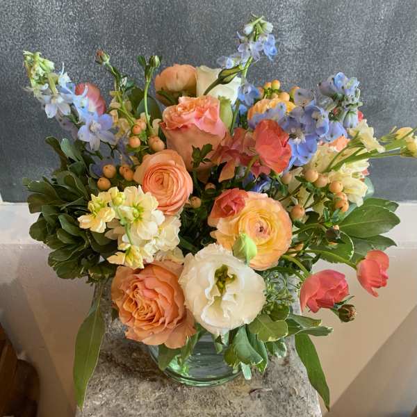 Mixed bouquet of peach, white, and blue flowers in a glass vase