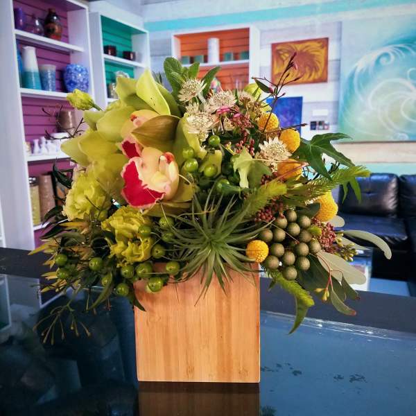 Mixed floral arrangement in a wooden cube vase with green and yellow blooms