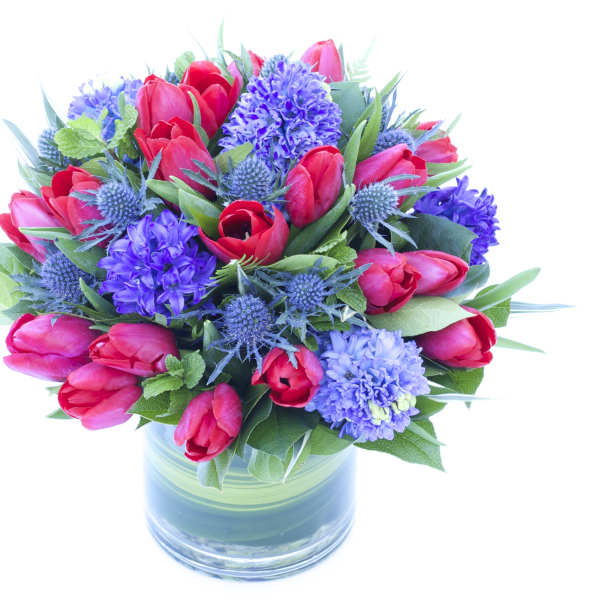 Bouquet of red tulips and purple flowers in a glass vase