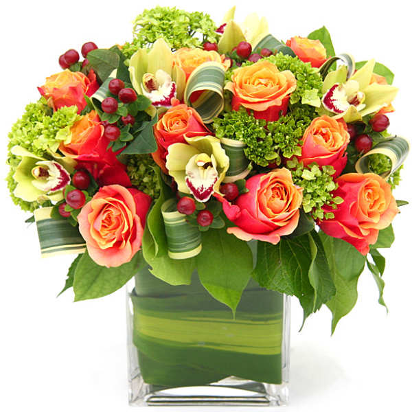 Orange roses and pale green orchids in a clear square vase