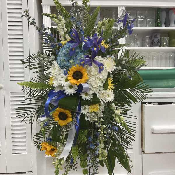Tall standing floral spray with sunflowers, white daisies, and blue flowers