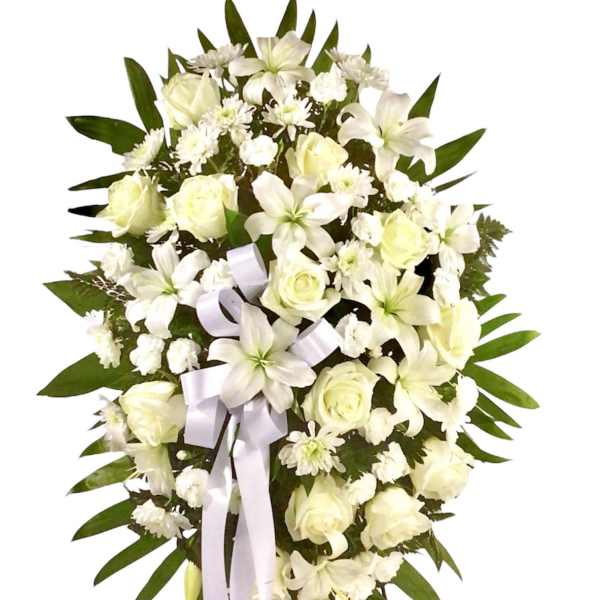 White floral standing spray with roses and lilies, accented by a pale ribbon