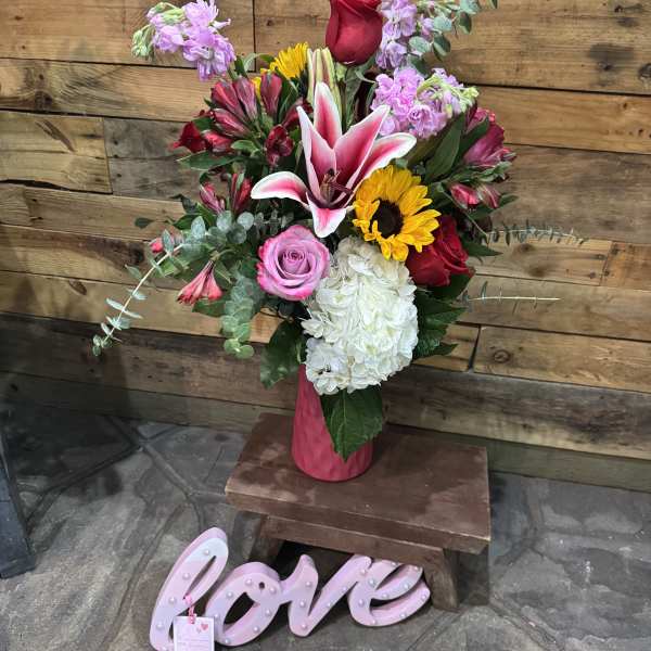 Mixed bouquet in a pink vase with a pink "love" sign below