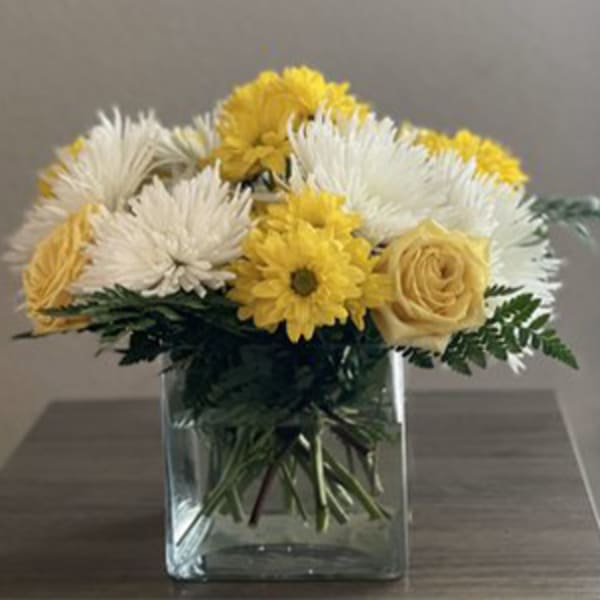 Yellow and white flowers arranged in a clear square vase