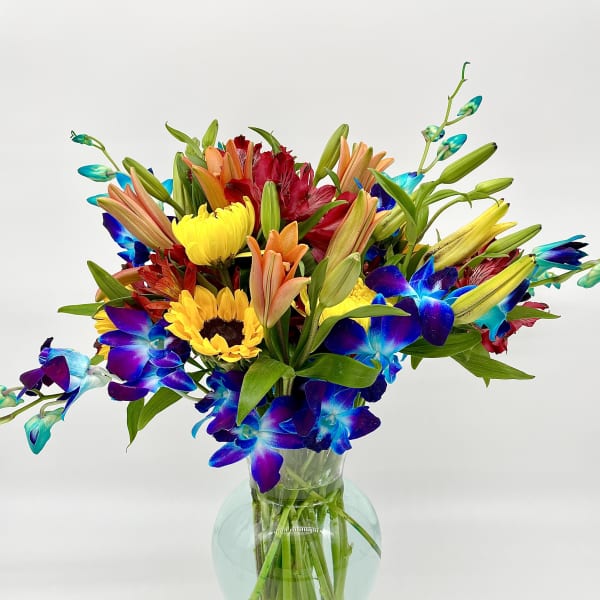 Colorful bouquet of lilies, sunflowers, and blue orchids in a glass vase
