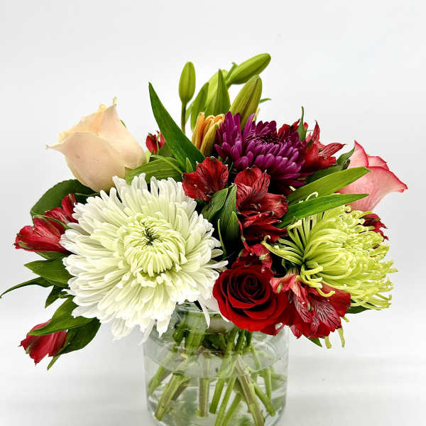 Mixed bouquet of roses, chrysanthemums, and lilies in a glass vase