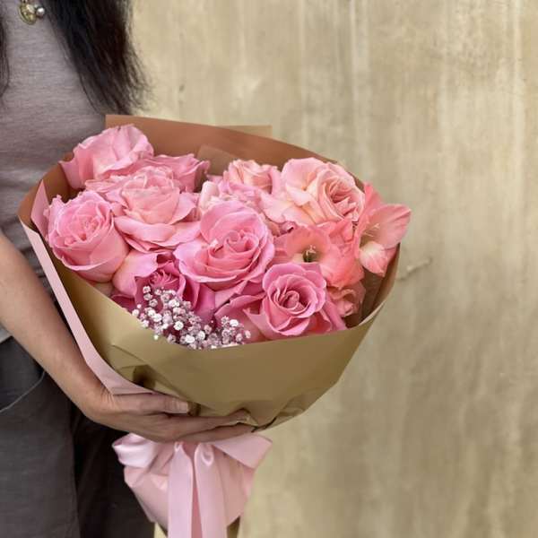 Pink rose bouquet wrapped in brown paper with a pink ribbon