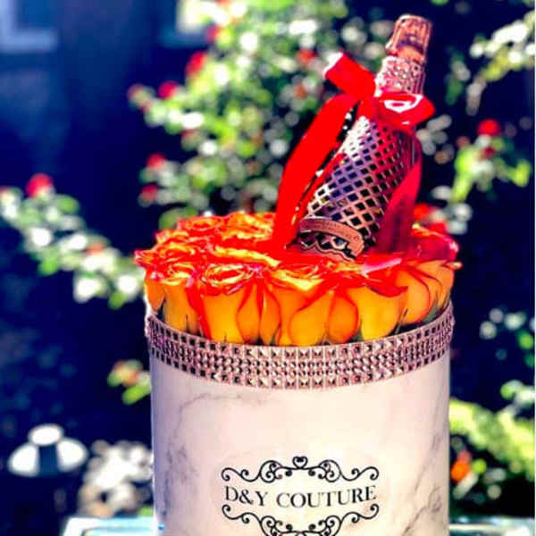 Round box of orange roses with a decorative bottle on top