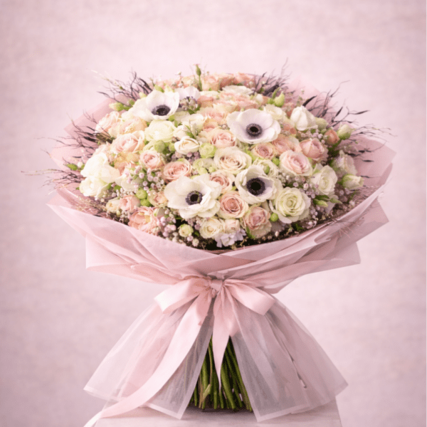 Large pastel bouquet of roses and white anemones wrapped in pink paper