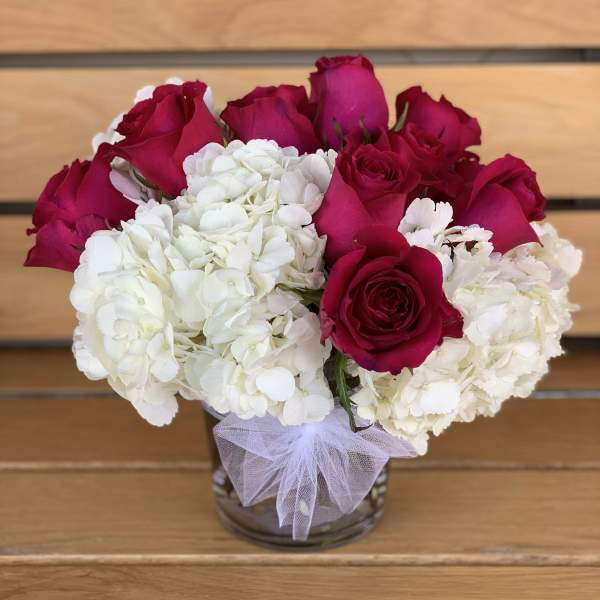 Red roses and white hydrangeas in a glass vase with a tulle bow