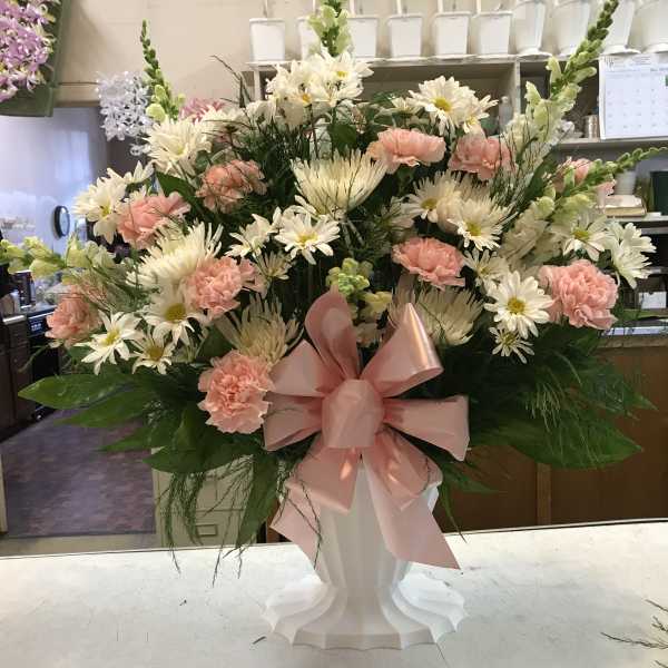 Pink and white mixed flower arrangement in a white pedestal vase with a pink bow