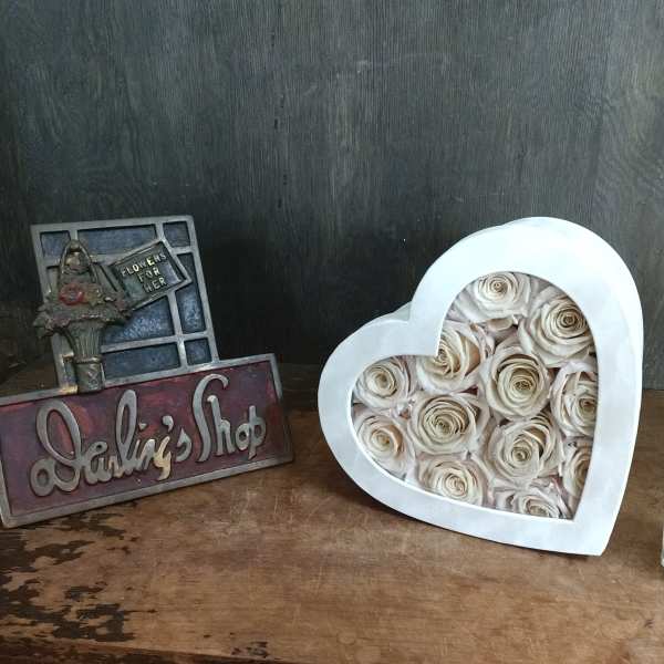 Heart-shaped box filled with cream roses beside a decorative shop sign