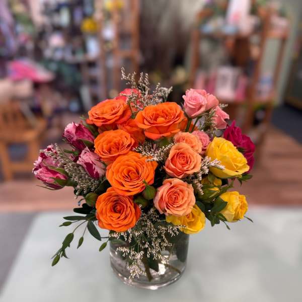 Mixed bouquet of orange, pink, and yellow roses with white filler flowers in a clear glass vase