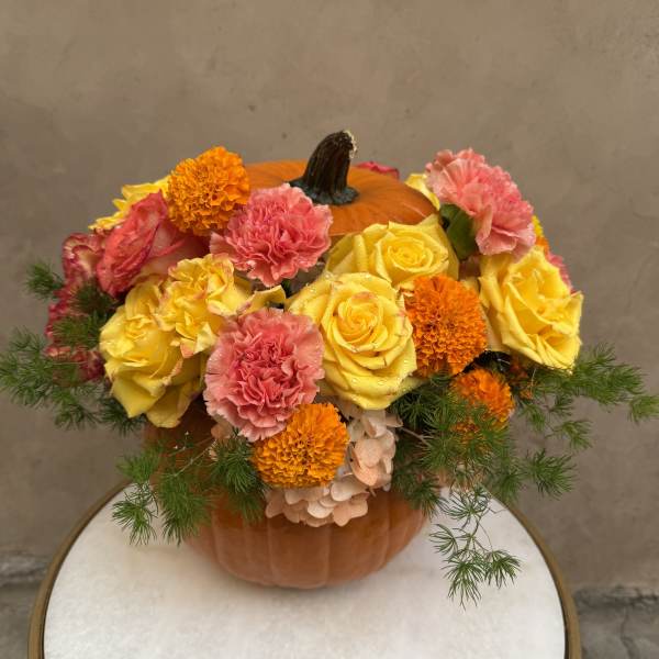 Pumpkin centerpiece with yellow roses, pink carnations, and orange marigolds