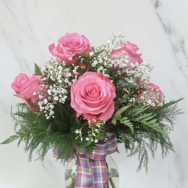 Pink roses in a glass vase with baby's breath and a plaid ribbon