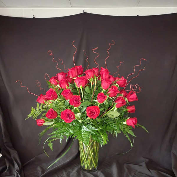 Red roses arranged in a clear glass vase with curly wire accents
