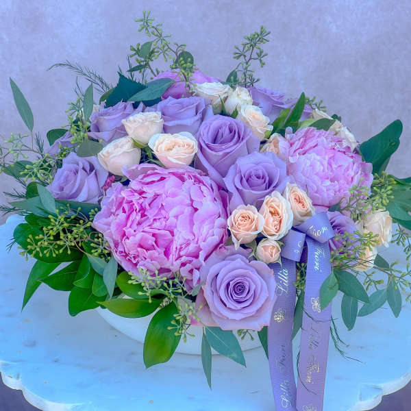Lavender roses and pink peonies in a white vase with purple ribbons