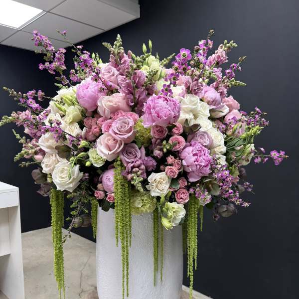 Tall arrangement of pink and white roses and peonies with trailing green accents in a white vase