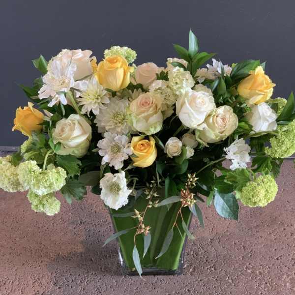 Yellow and white roses in a clear vase with mixed white blooms