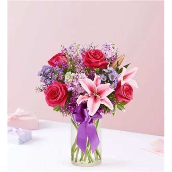 Pink roses and lilies in a clear glass vase with a purple ribbon